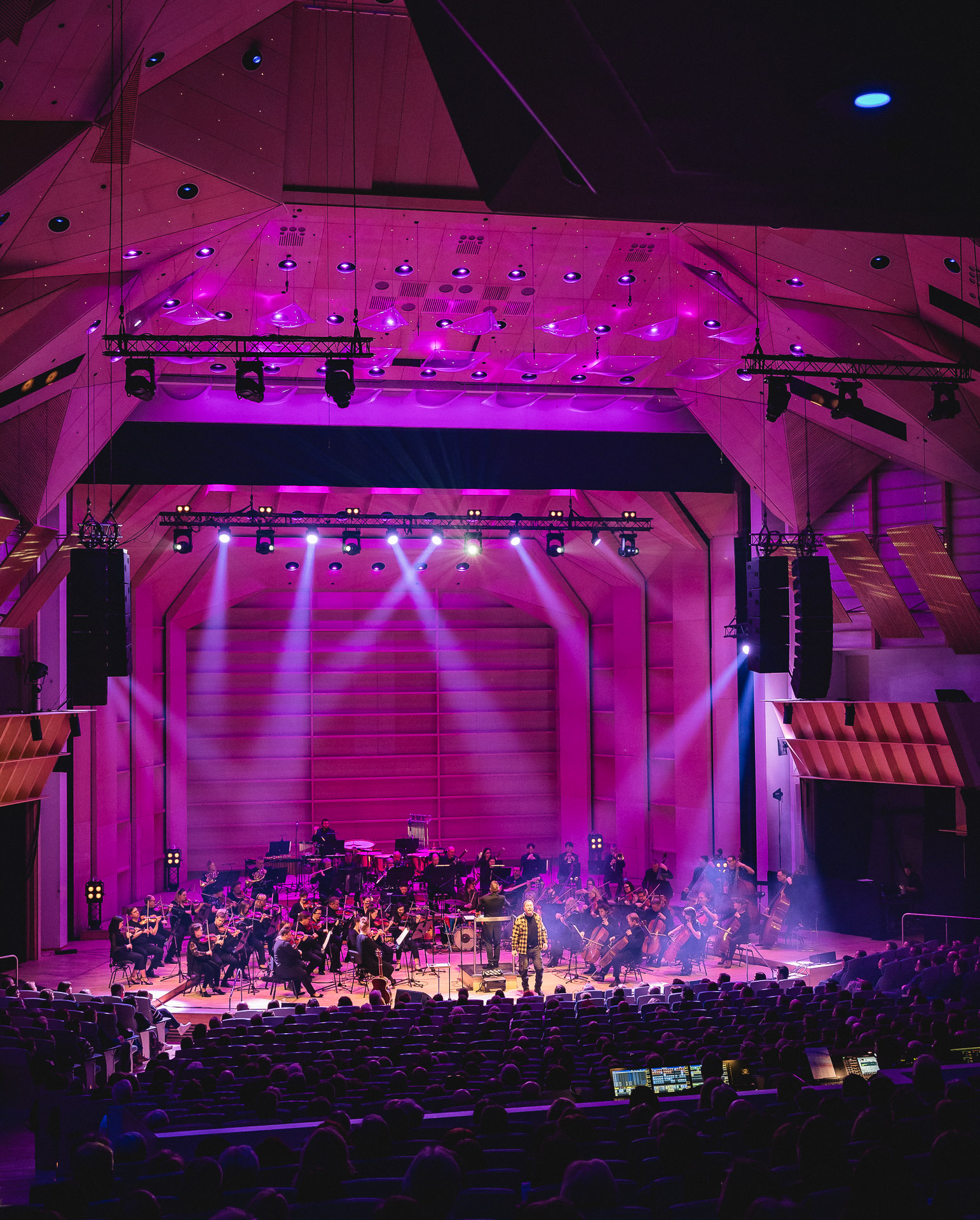 Magentan ja sinisen valaistuksen täyttämä konserttisali, jossa orkesteri esiintyy yleisön edessä